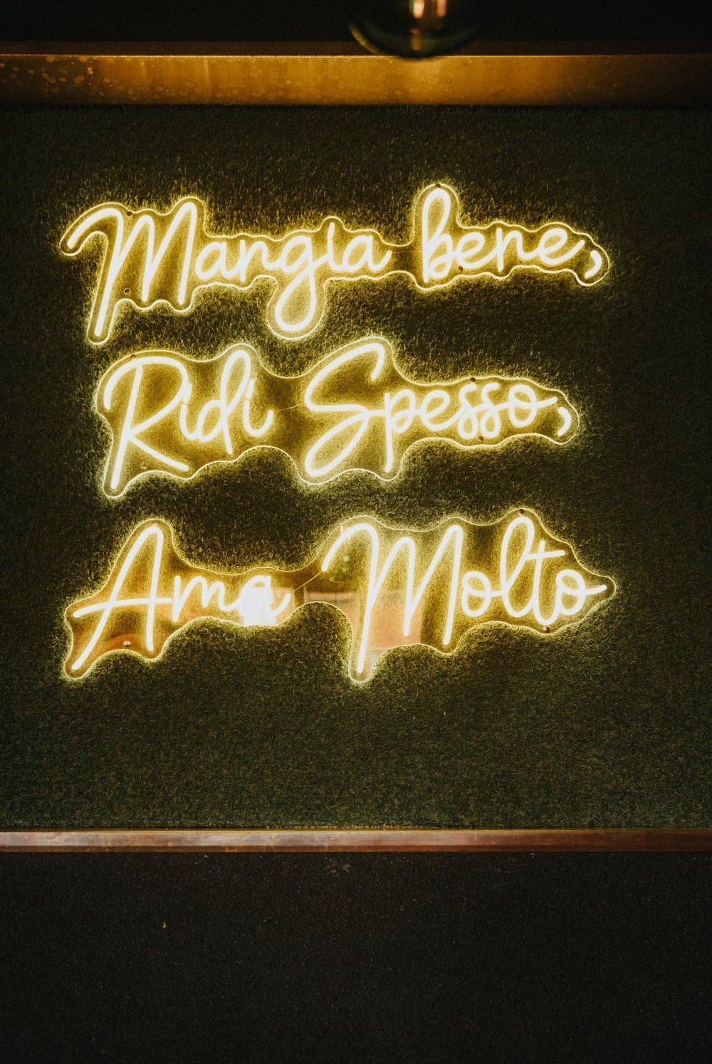 Grünes LED-Neonschild mit dem Schriftzug Mangia Bene Ridi Spesso in einem Restaurant