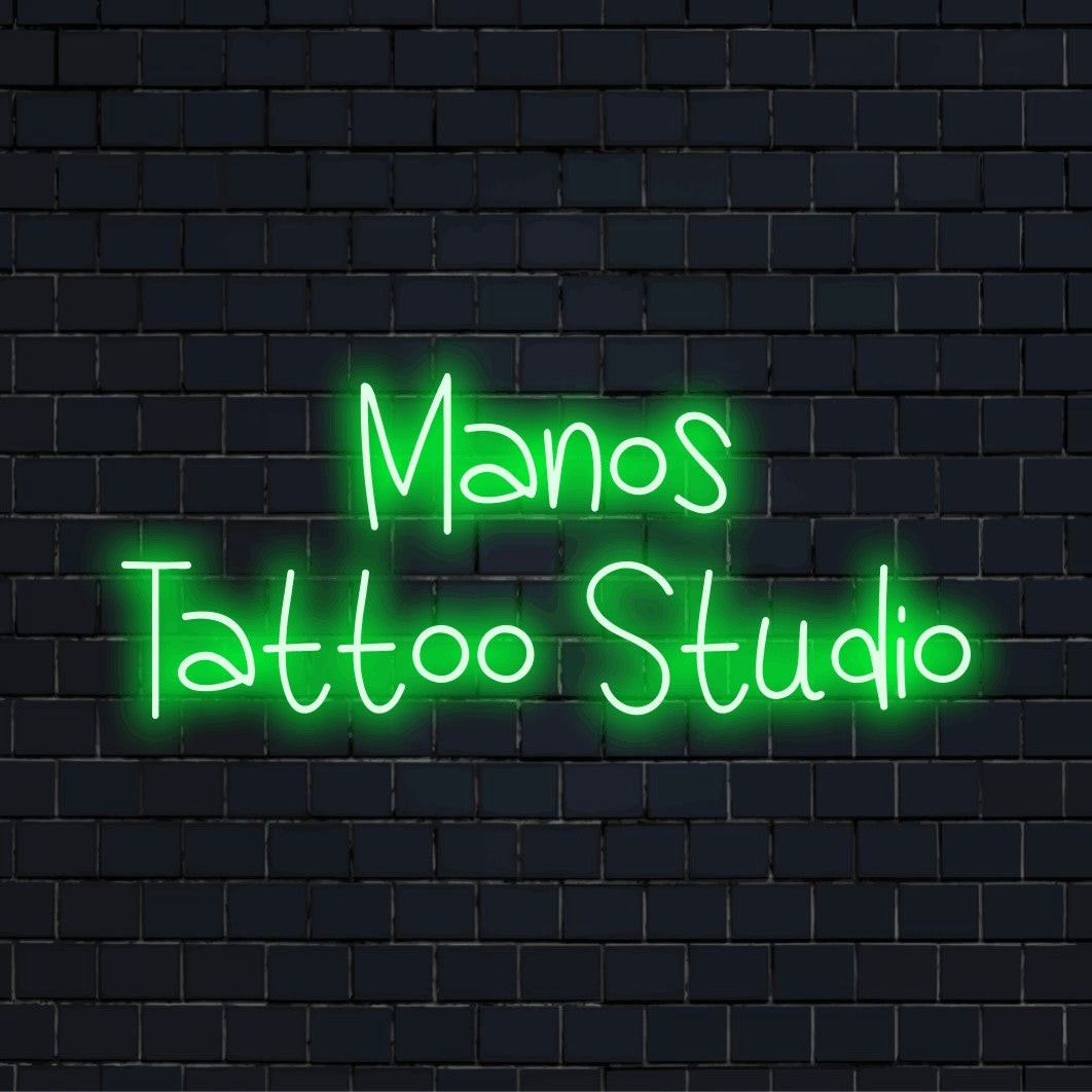 Manos Tattoo Studio Custom Name Neon Sign, neon text light against black brick wall