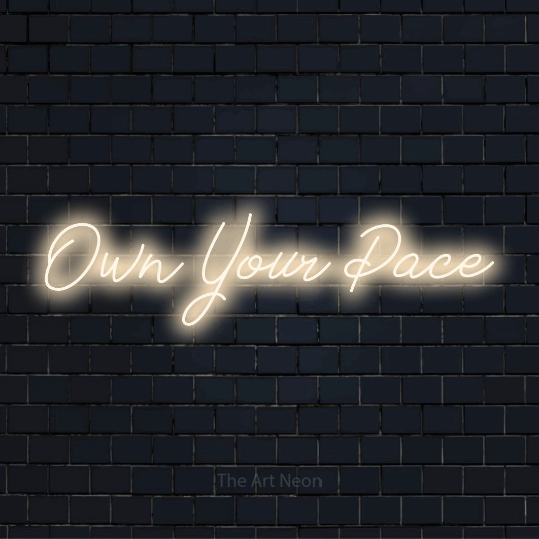 "Own Your Pace" glowing LED neon sign on a black brick wall
