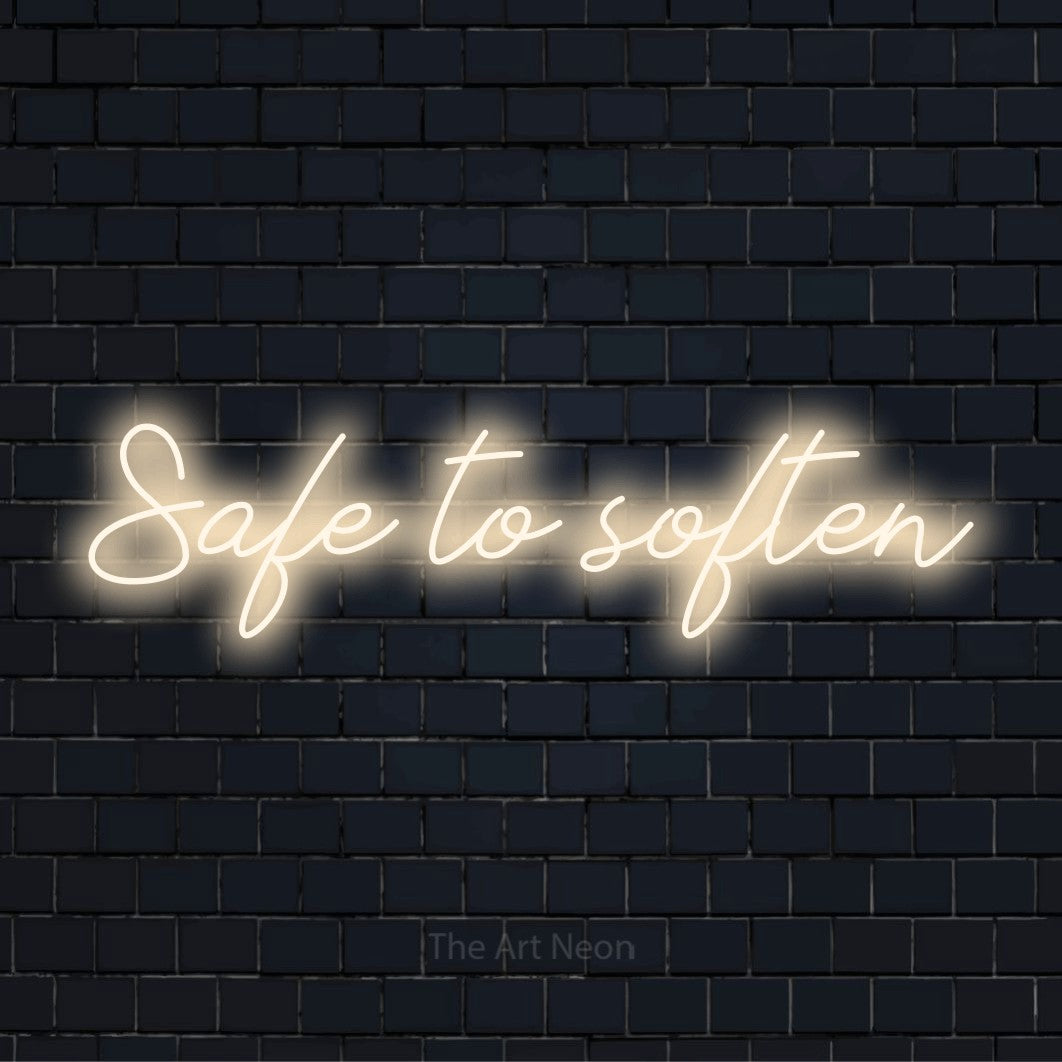 "Safe To Soften" glowing LED neon sign on a black brick wall