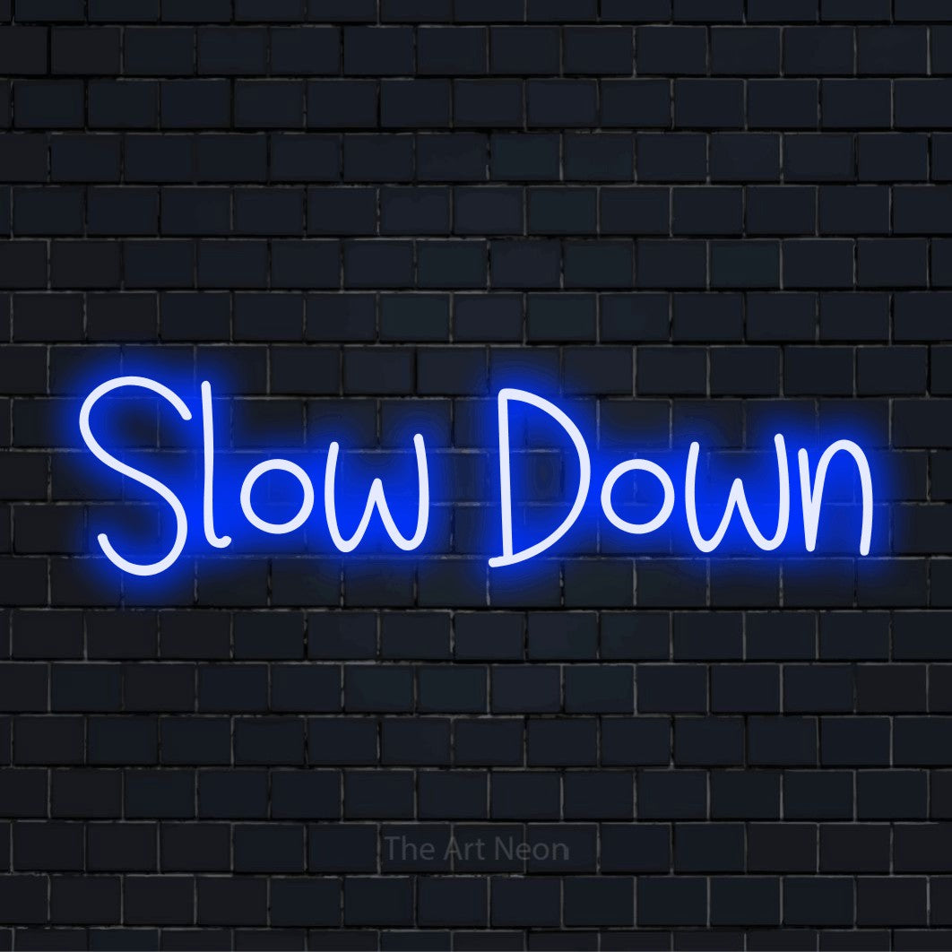 "Slow Down" glowing LED neon sign on a black brick wall