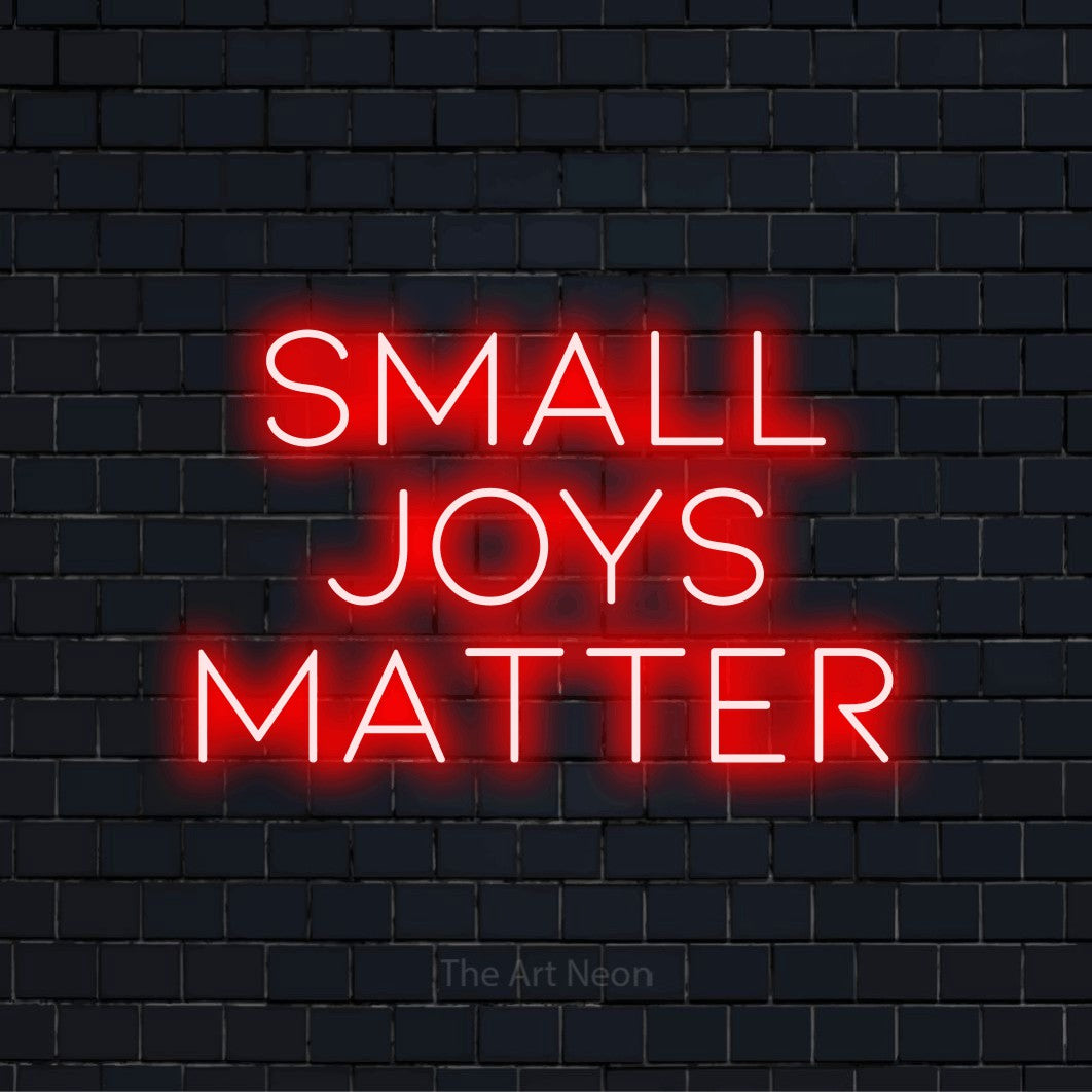 "Small Joys Matter" glowing LED neon sign on a black brick wall