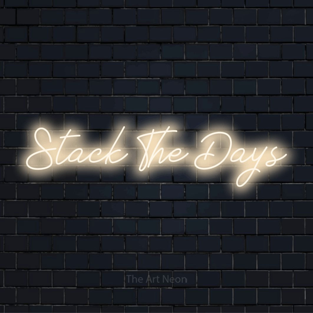 "Stack The Days" text design with neon effect on a black brick wall