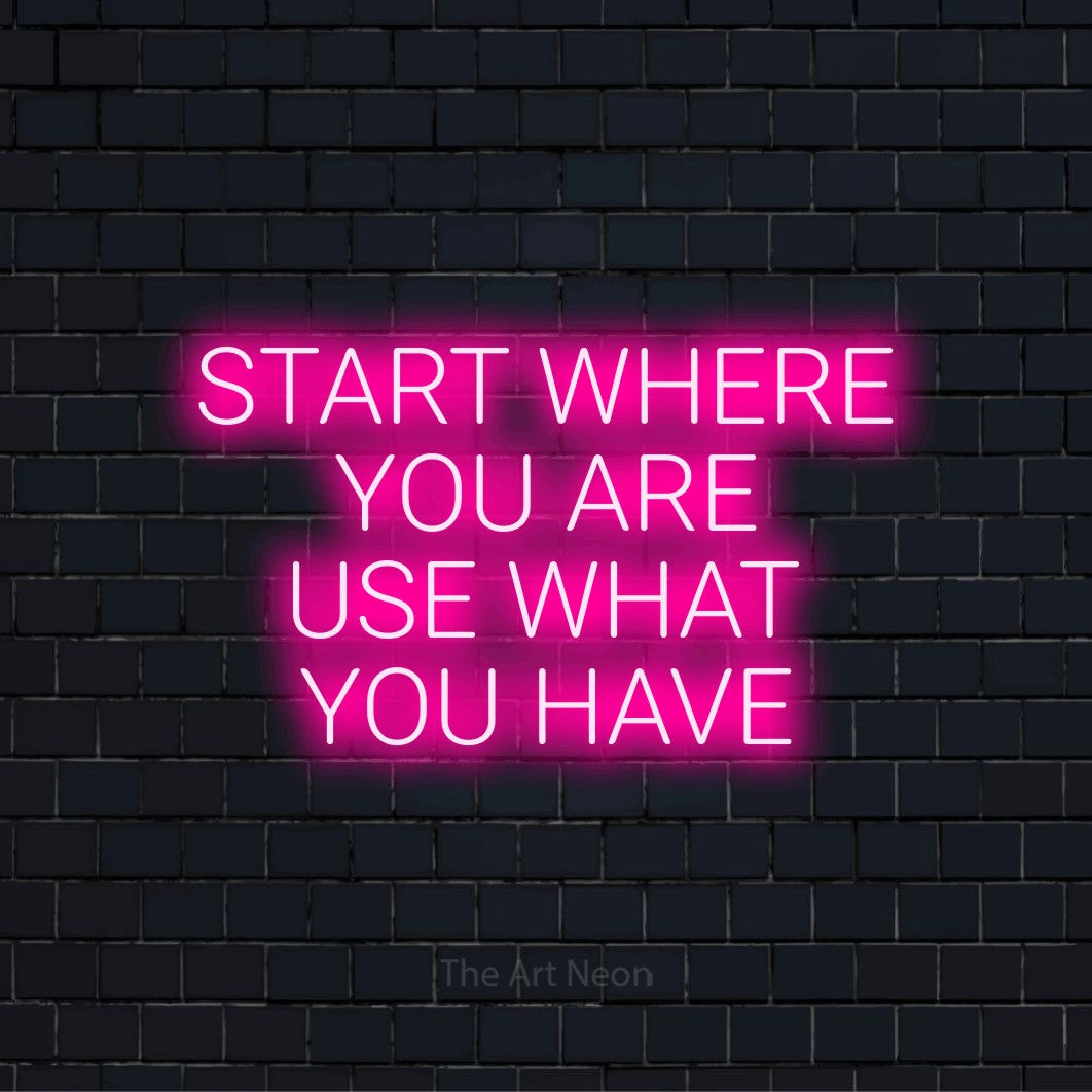 "Start Where You Are Use What You Have" neon text design on a black brick wall