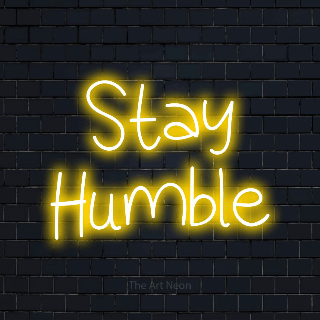 "Stay Humble" script-style LED neon sign on a black brick wall