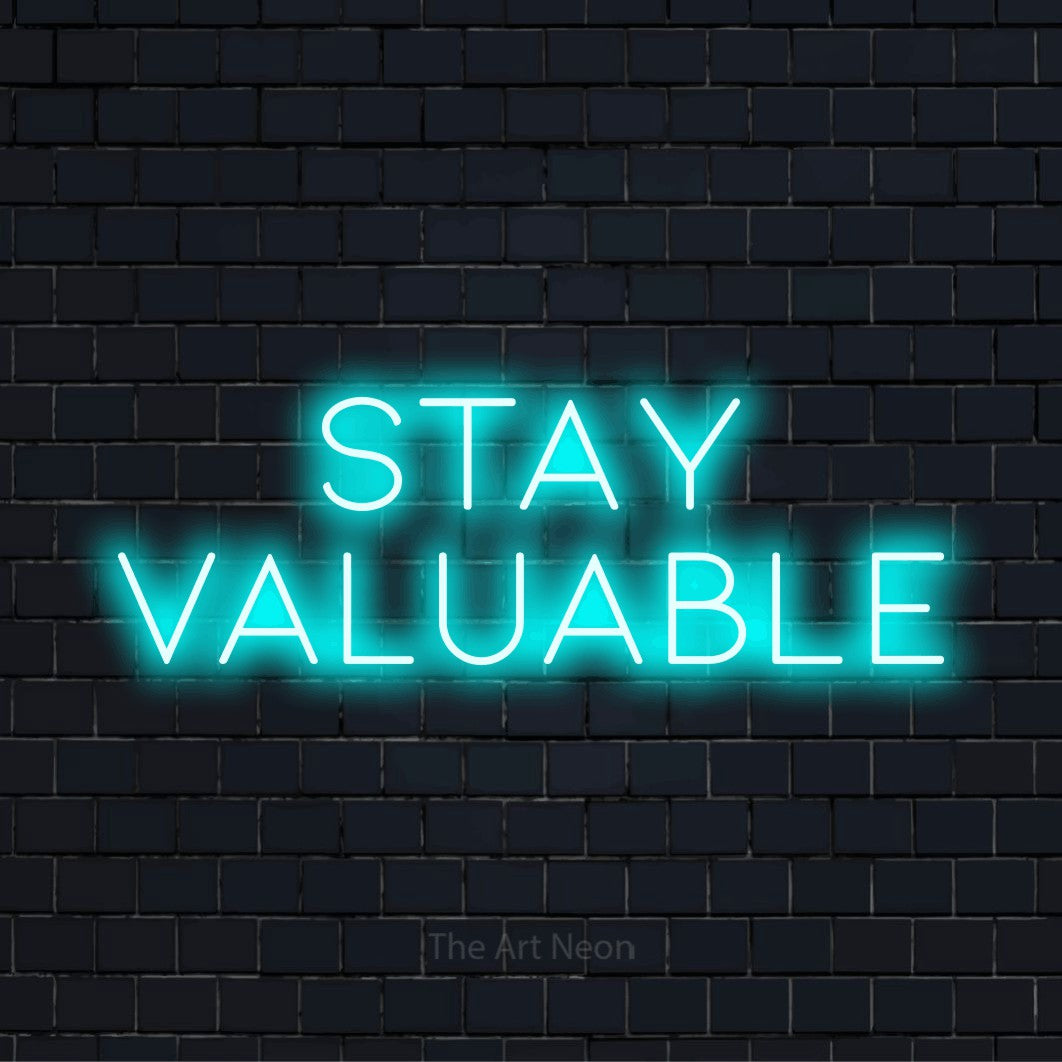 "Stay Valuable" script-style LED neon sign on a black brick wall