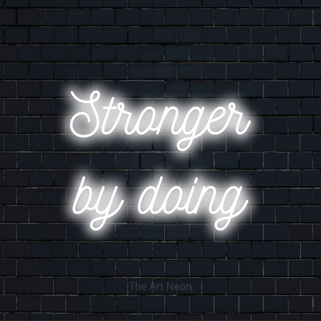 "Stronger By Doing" glowing LED neon sign on a black brick wall