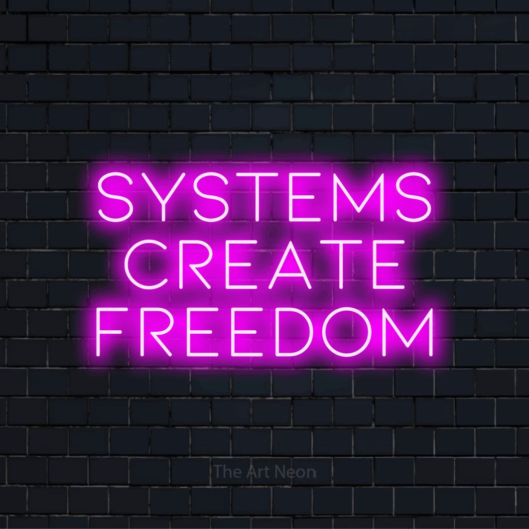 "Systems Create Freedom" text design with neon effect on a black brick wall