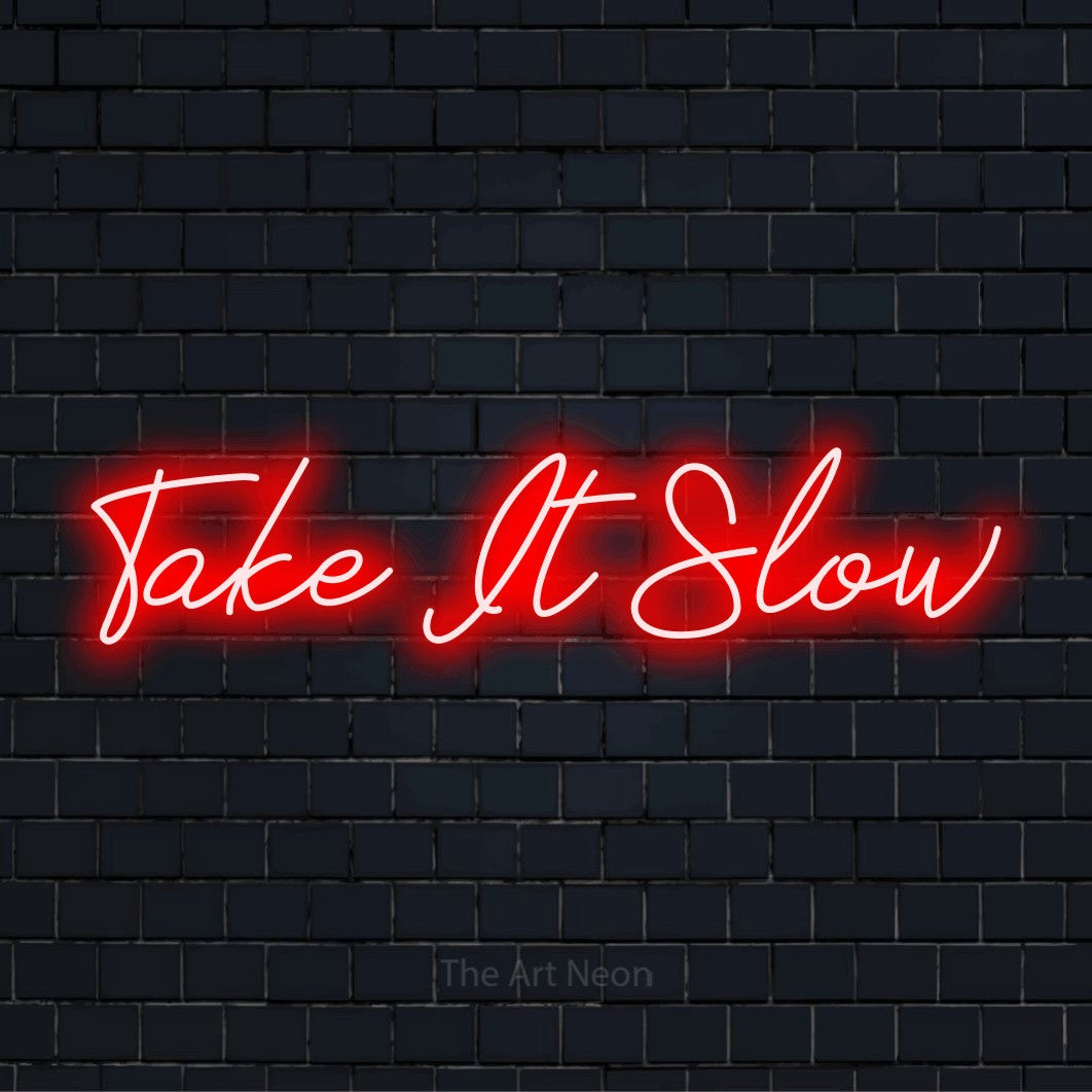 "Take It Slow" text design with neon effect on a black brick wall