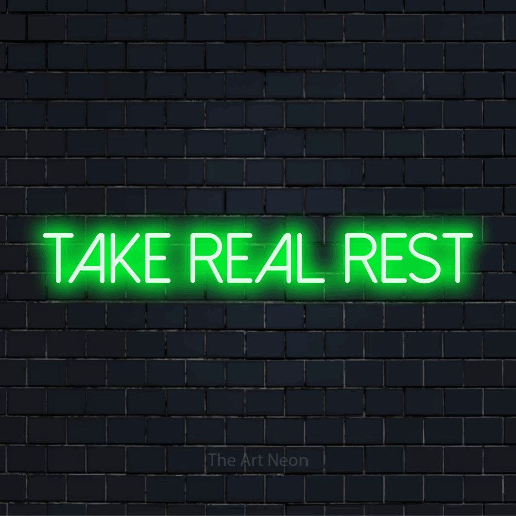 "Take Real Rest" script-style LED neon sign on a black brick wall