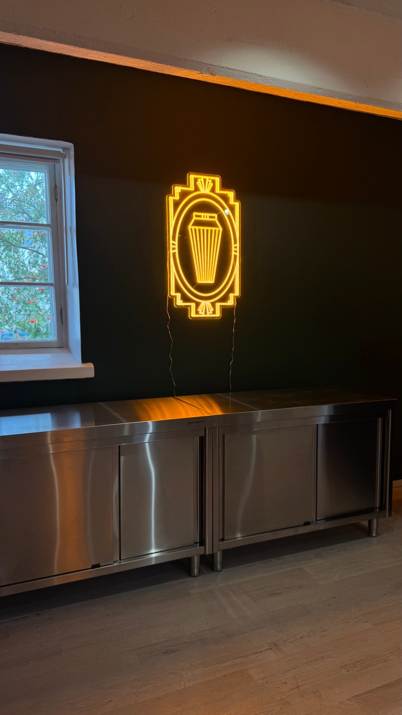 Warm-yellow cocktail shaker icon LED neon in an Art Deco frame on a dark wall.