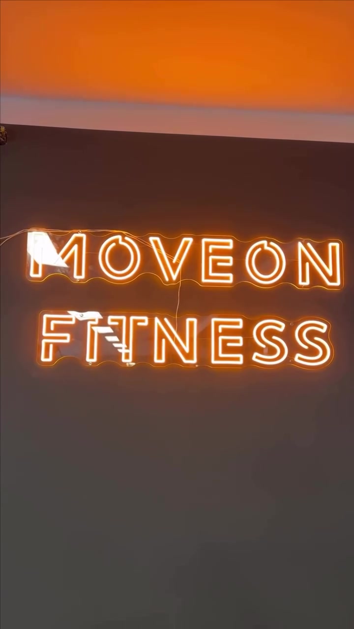 Warmgelbes LED-Neonlogo MOVEON FITNESS an einer dunklen Studiowand