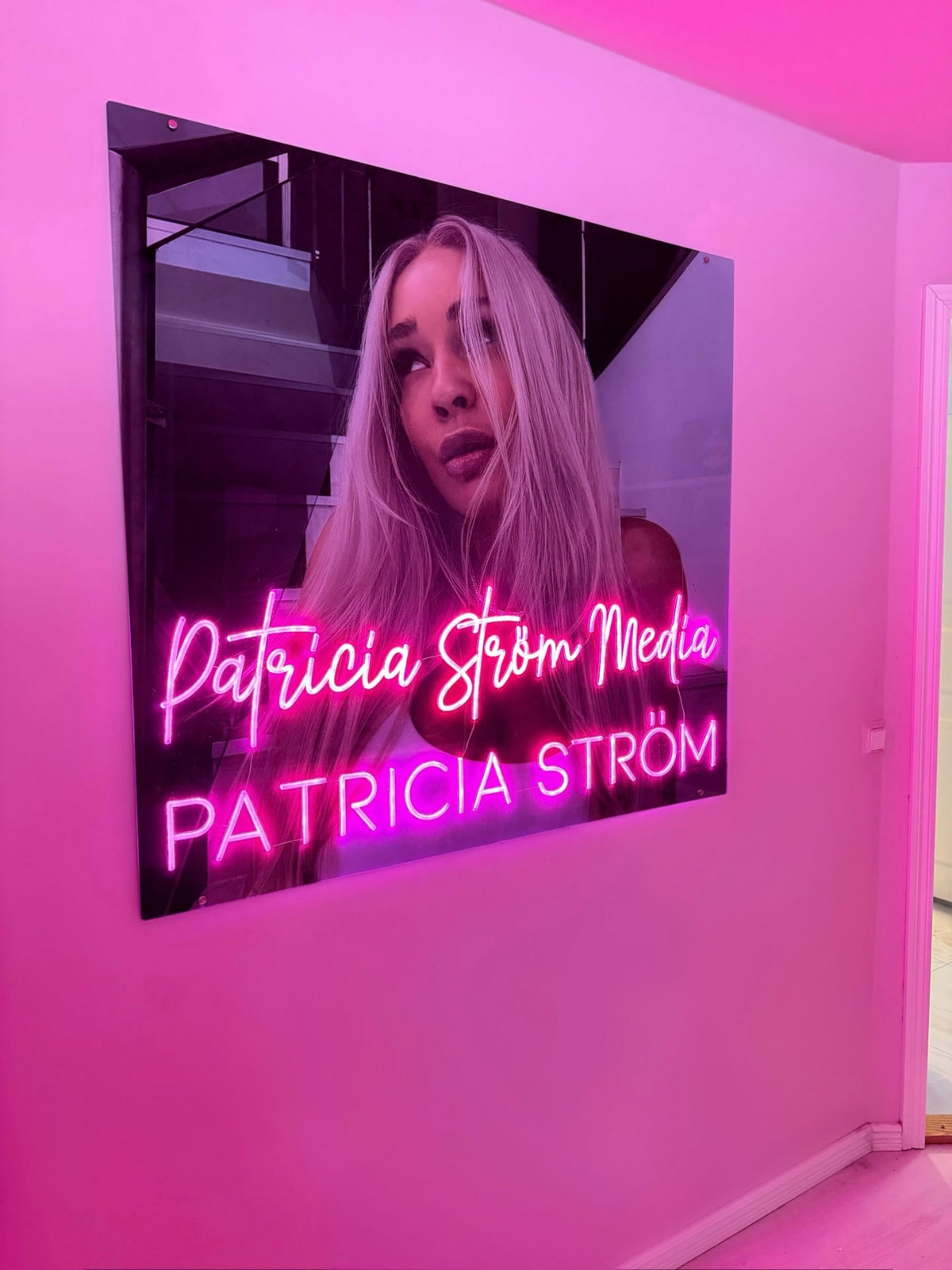 Pink Patricia Ström Media neon logo displayed beside Patricia Ström in her branded workspace