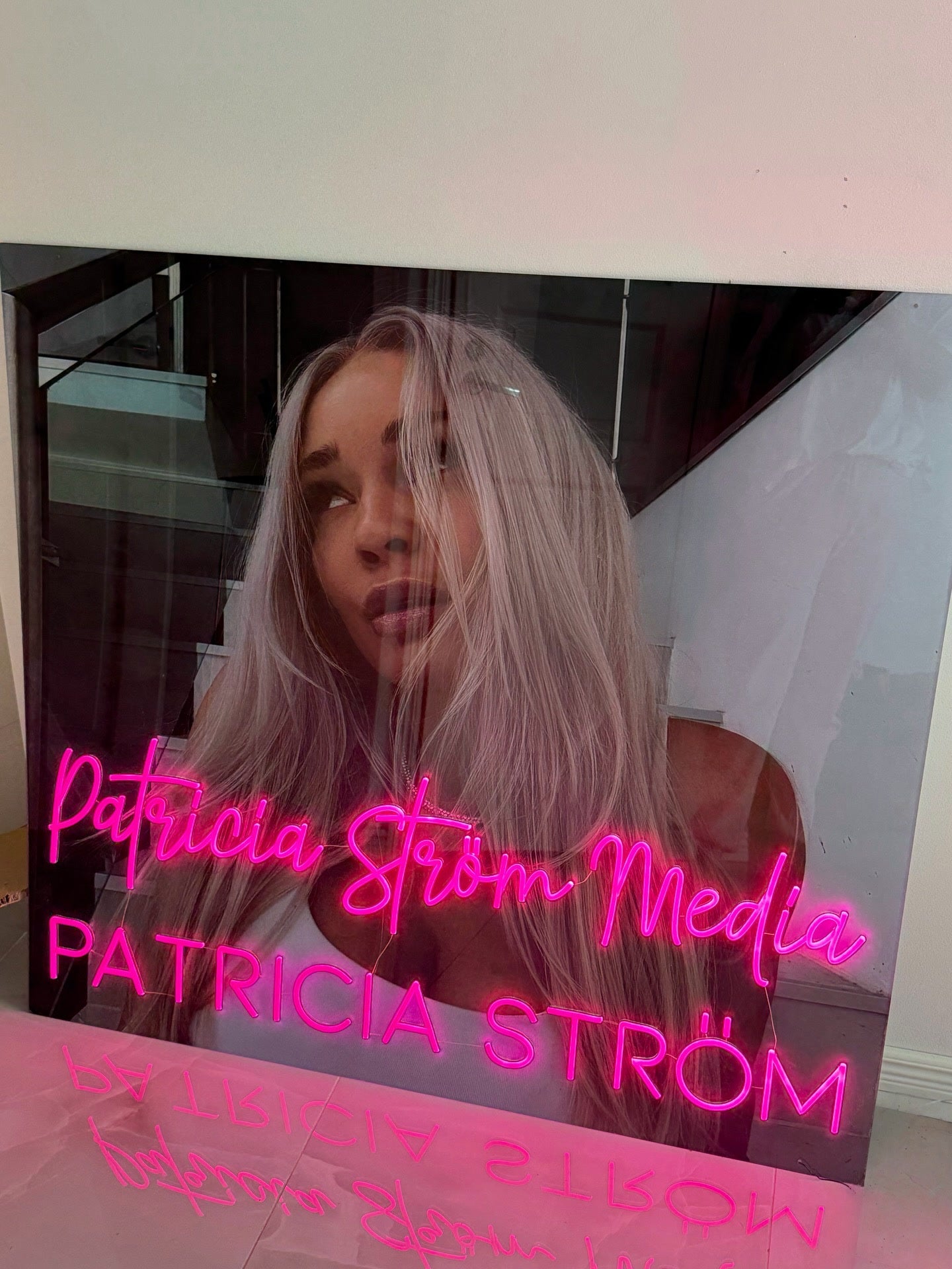 Pink Patricia Ström Media neon logo displayed beside Patricia Ström in her branded workspace