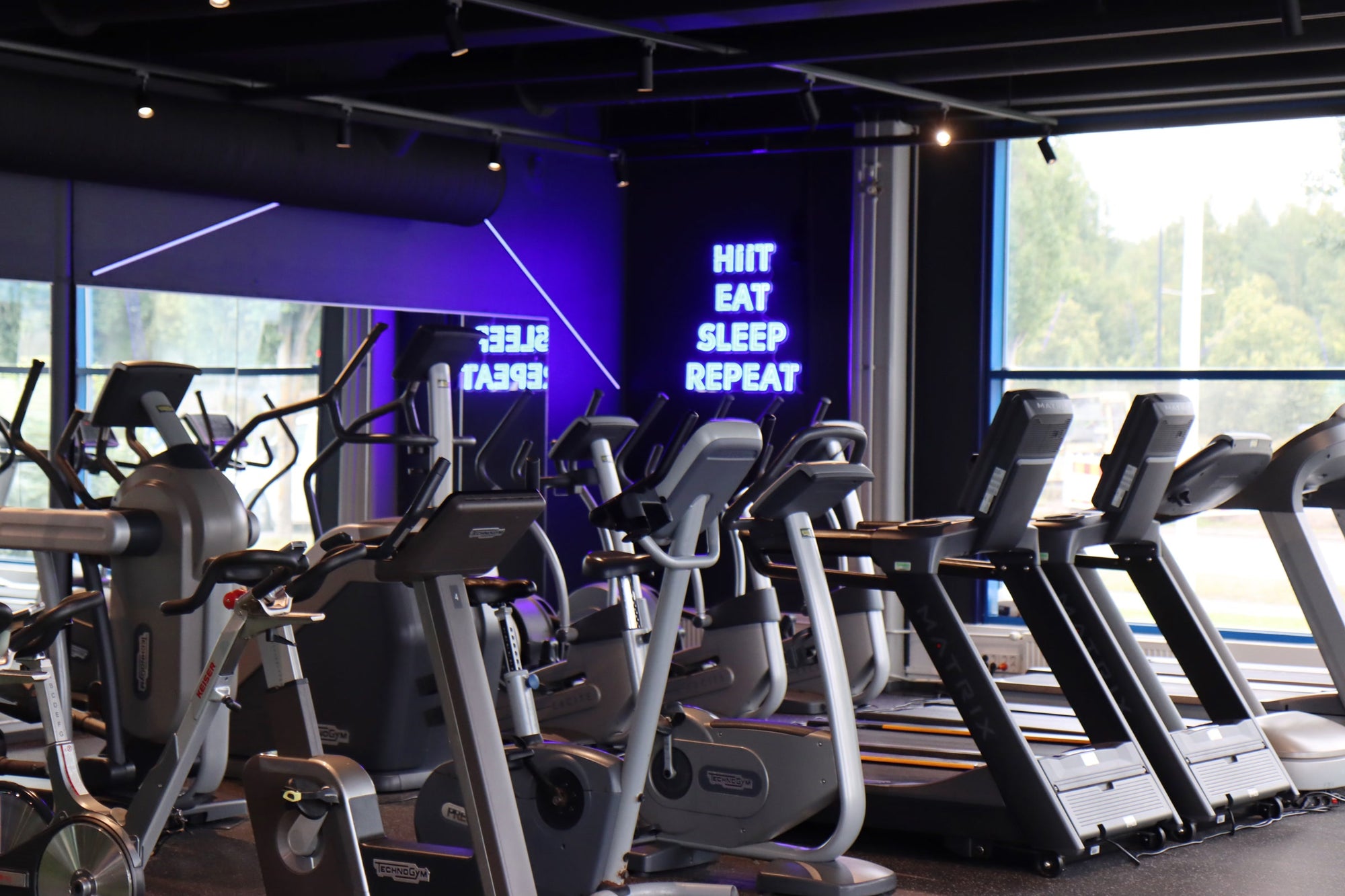 Innenraum des Fitnessstudios Kuntomaailma mit einem blauen LED-Neonschild im Verhältnis zum Raum