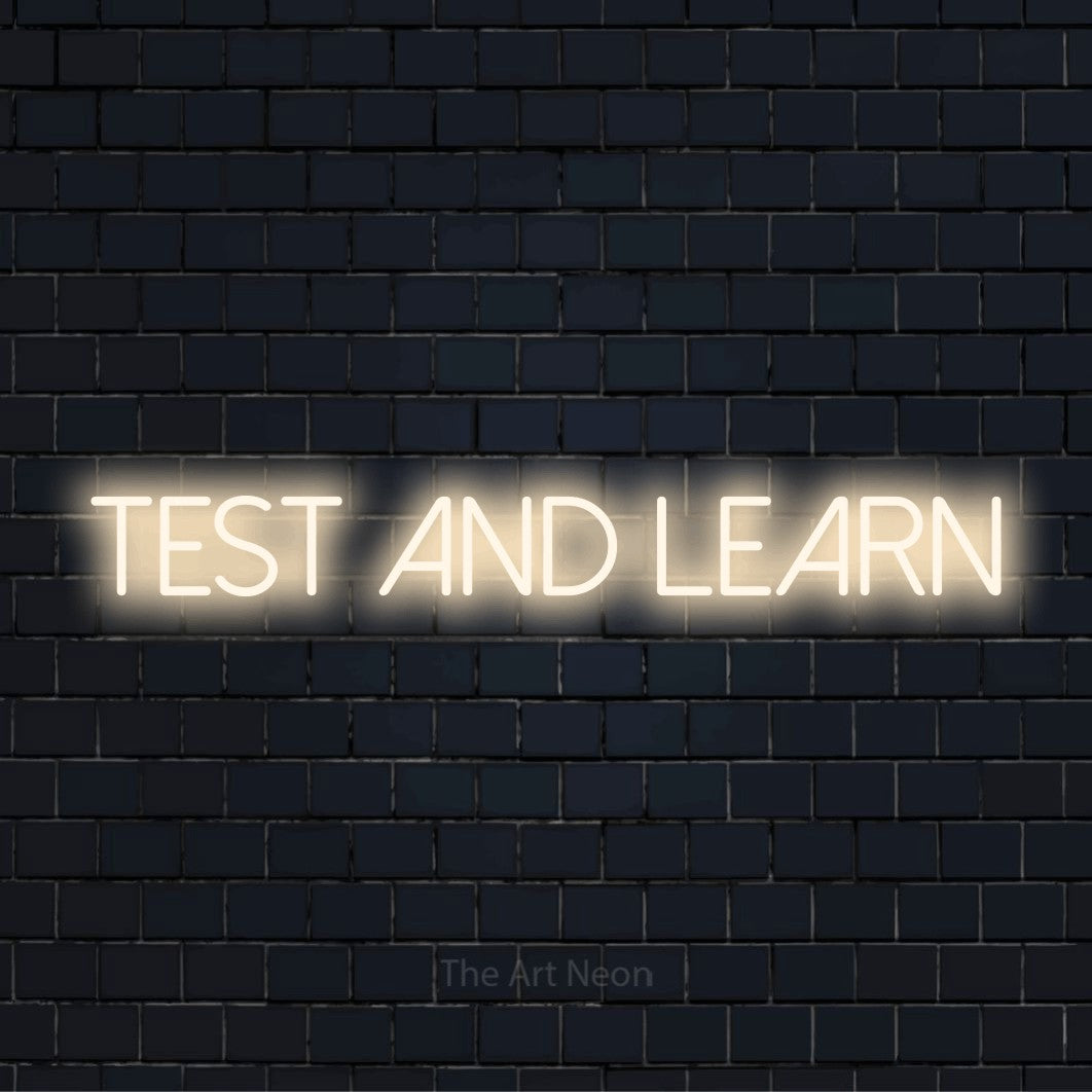 "Test And Learn" text design with neon effect on a black brick wall