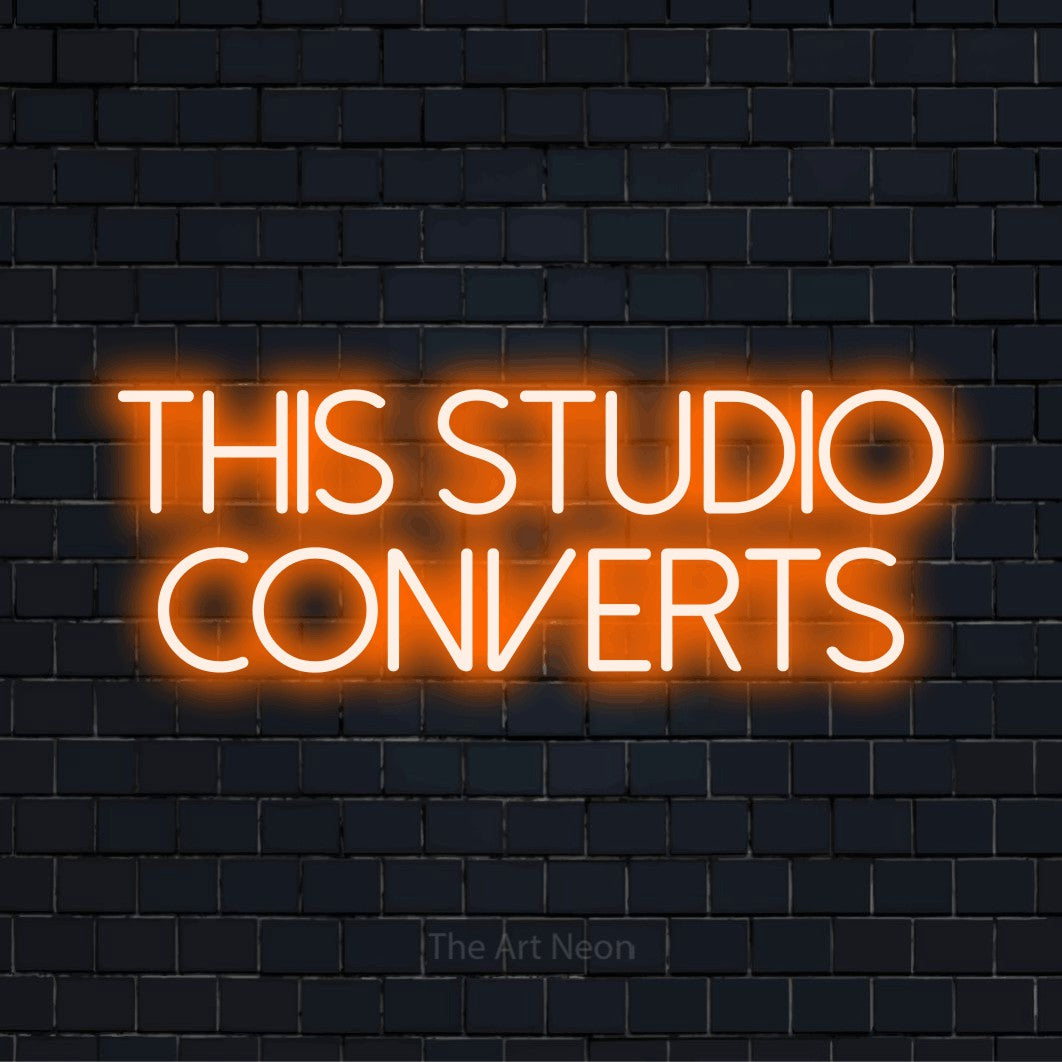 "This Studio Converts" glowing LED neon sign on a black brick wall