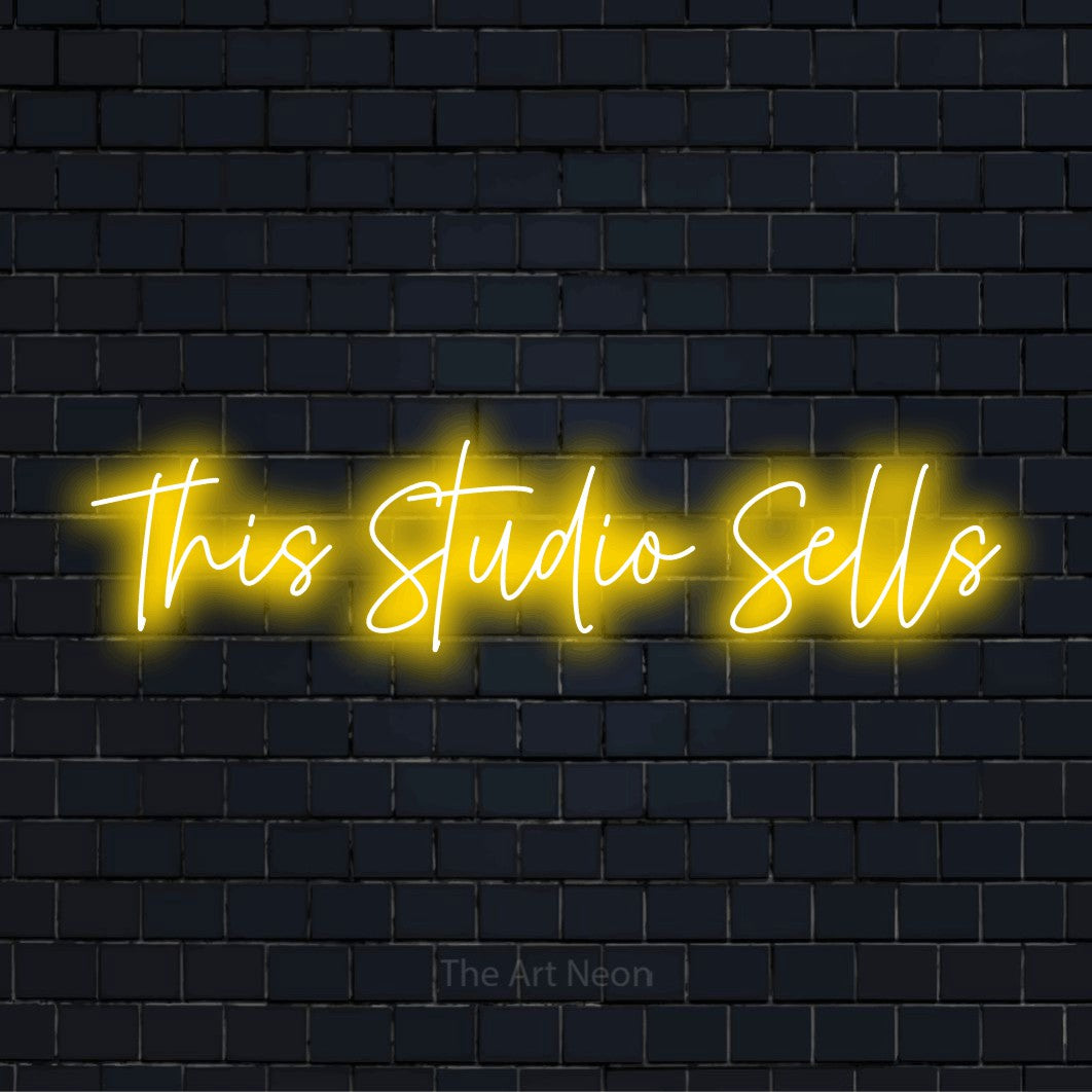 "This Studio Sells" neon text design on a black brick wall