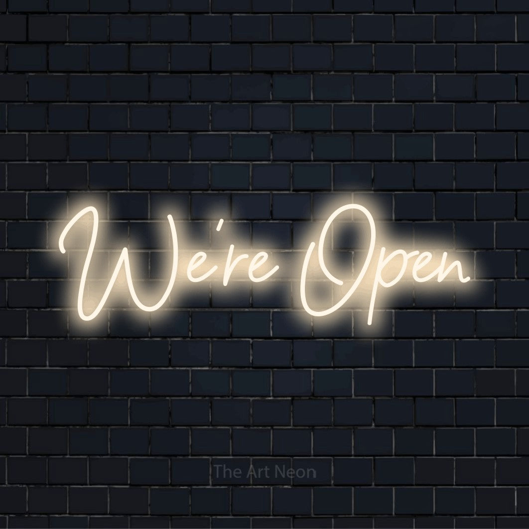 "We’re Open" glowing LED neon sign on a black brick wall
