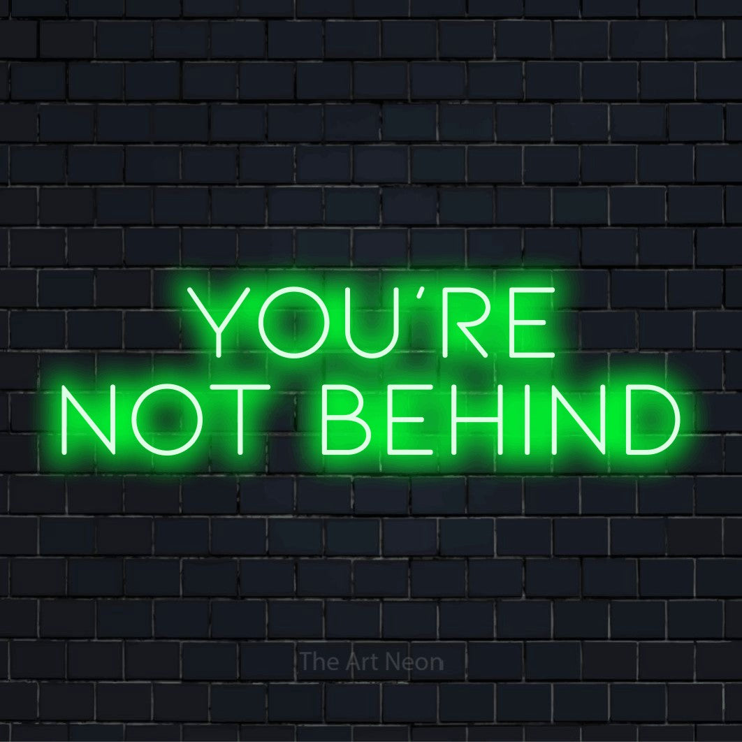 "You’re Not Behind" neon text design on a black brick wall